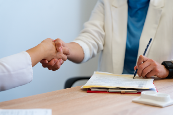 Deux personnes se serrent la main lors d'un entretien pour l'embauche d'un salarié, avec un contrat et des documents administratifs posés sur la table.